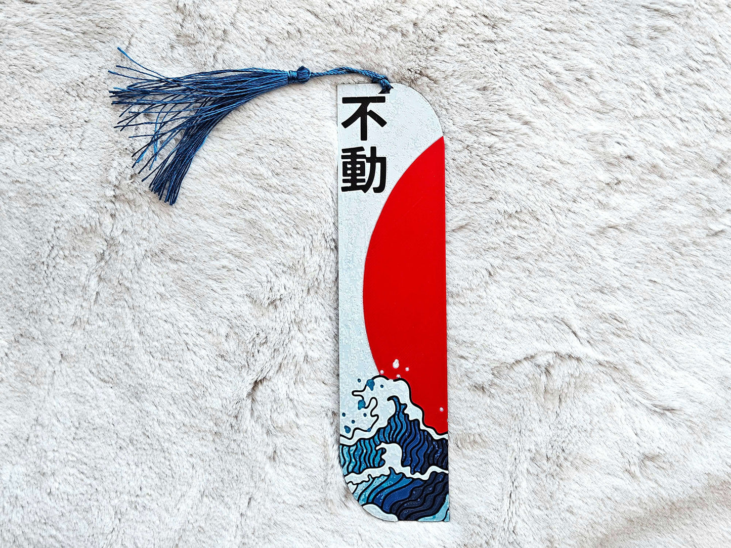Semn de carte „Unshakable” (不動) cu valuri și soare roșu, design japonez elegant.